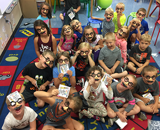 group of students sitting on the floor in their classroom, wearing silly glasses