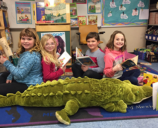 four student reading books on a stuffed alligator 